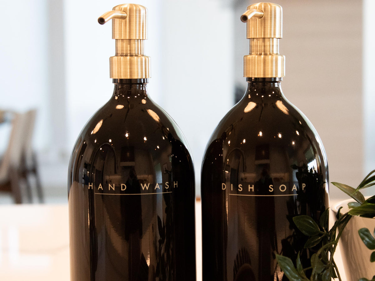 Refillable amber glass dish soap and hand wash dispensers with antique brass pumps on a kitchen counter