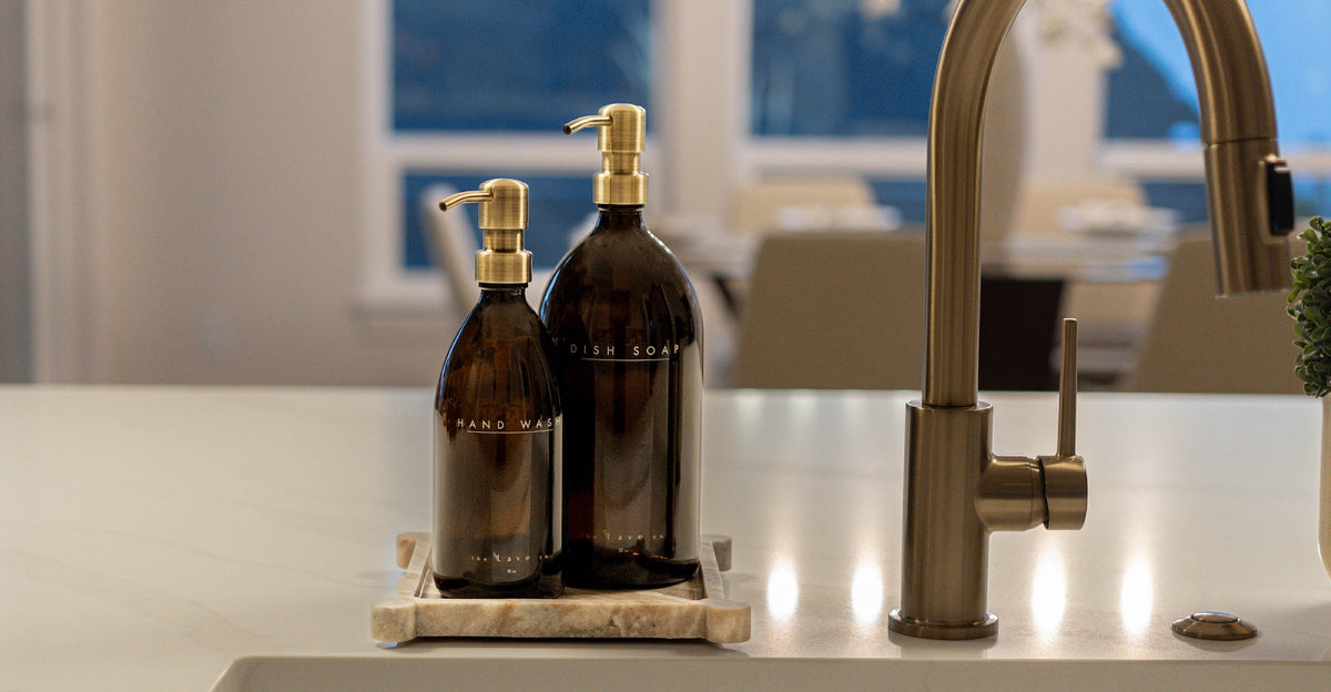 Amber glass hand wash and dish soap bottles with brass pumps beside a brass kitchen faucet